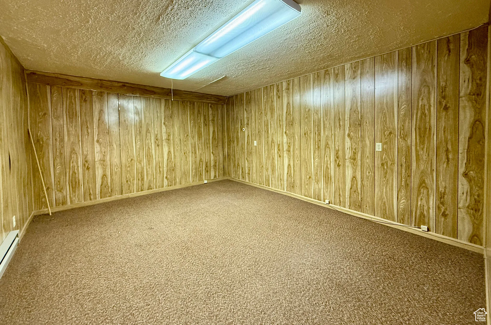 Carpeted spare room with wood walls, a baseboard radiator, and a textured ceiling