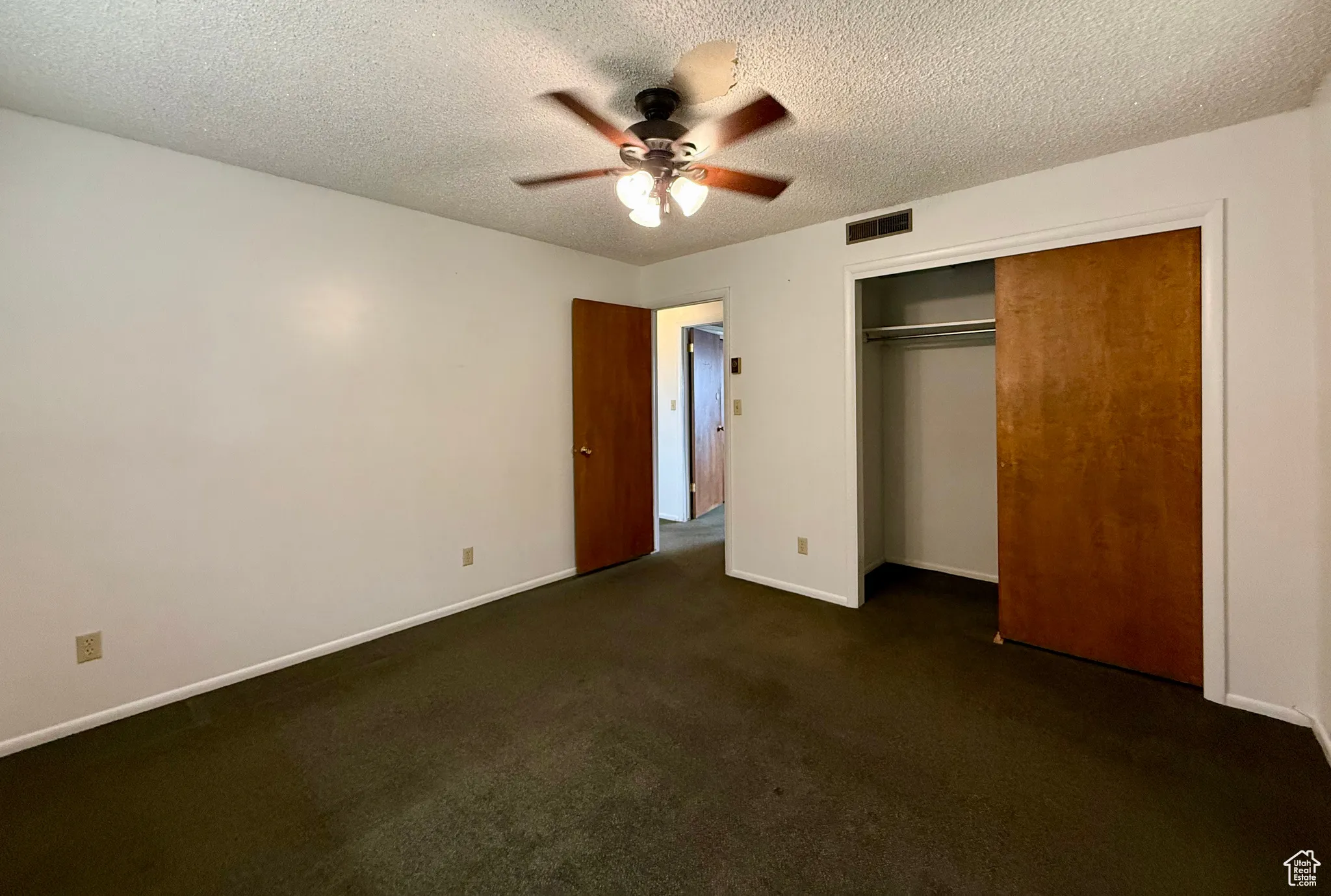 Unfurnished bedroom with dark carpet, a textured ceiling, a closet, and a ceiling fan