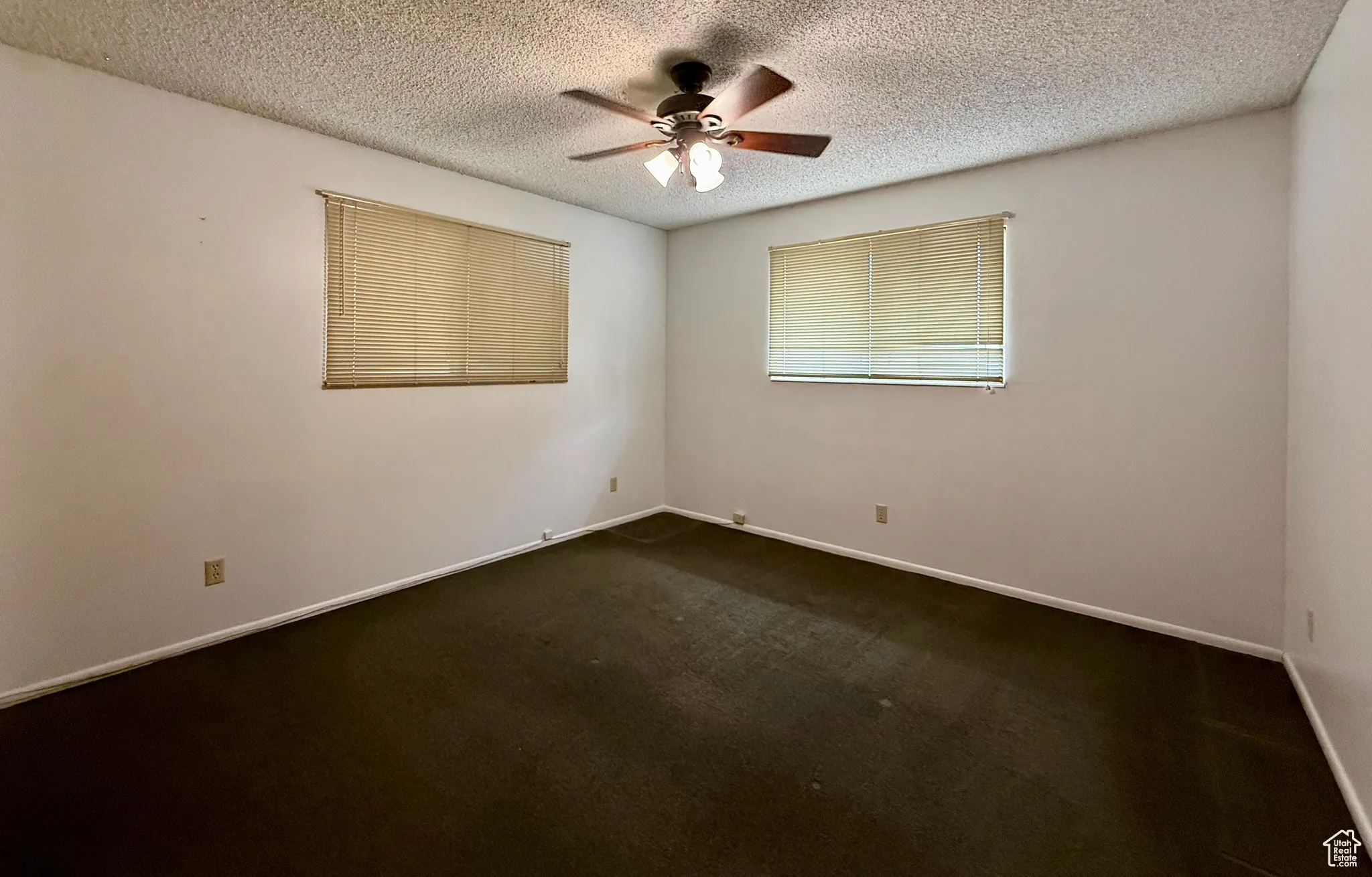 Spare room featuring dark carpet, a textured ceiling, and ceiling fan