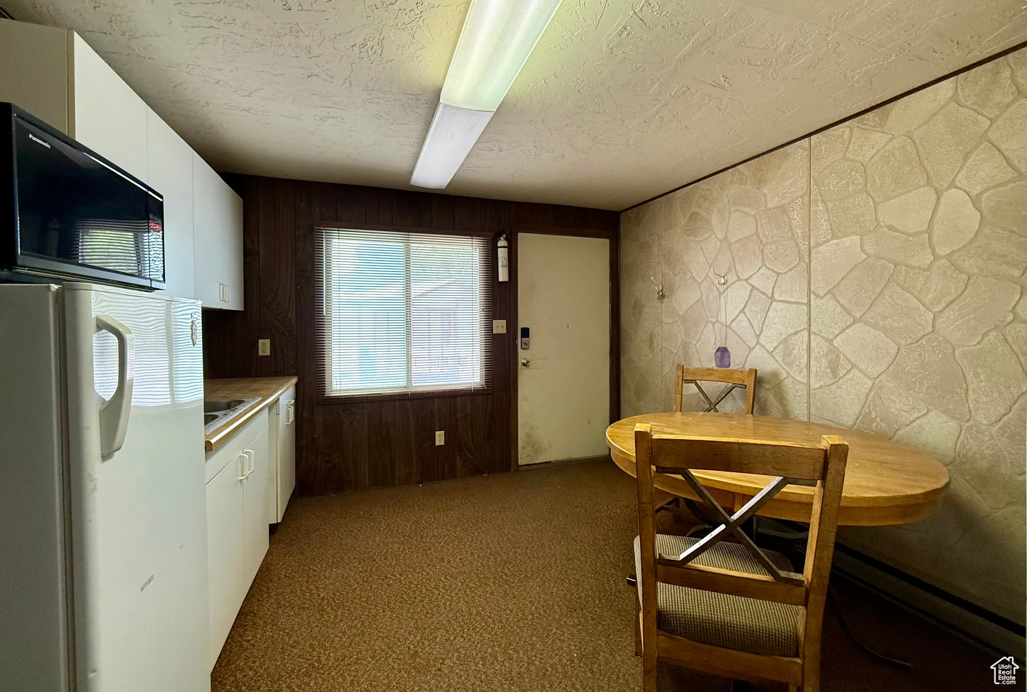 Kitchen with white cabinetry, white fridge, black microwave, light countertops, and dark carpet