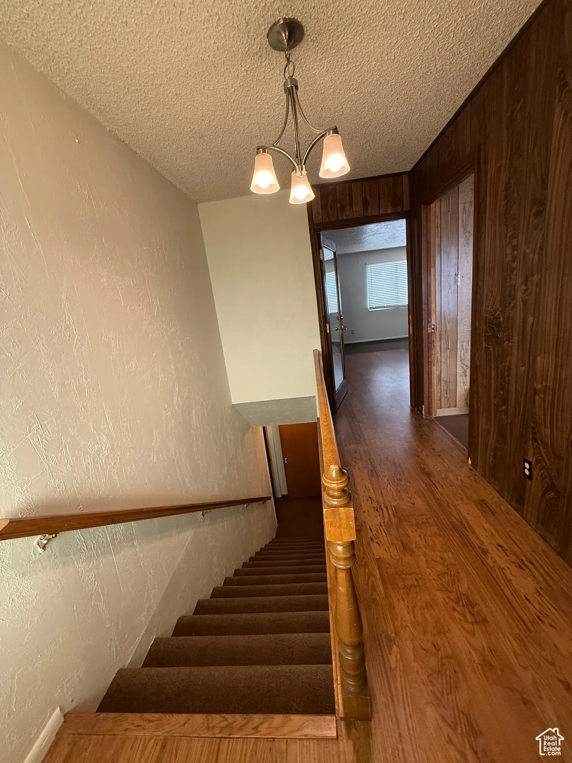 Staircase featuring a textured wall, wood finished floors, a textured ceiling, and a chandelier
