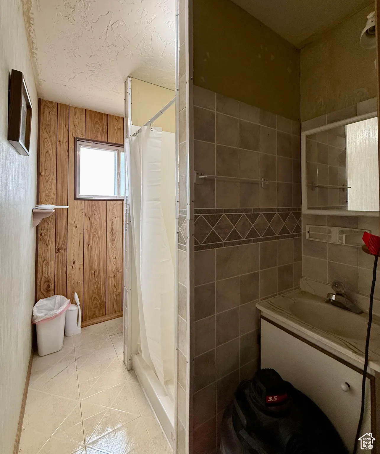 Full bathroom featuring light tile patterned flooring, vanity, a stall shower, tile walls, and a textured ceiling