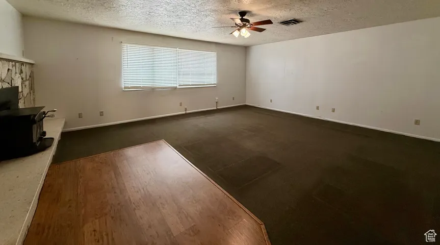 Unfurnished living room featuring a textured ceiling, dark wood-style flooring, a ceiling fan, and a wood stove