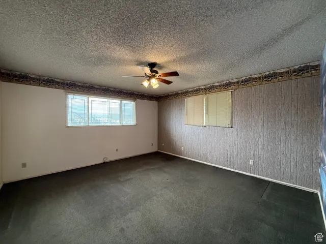 Unfurnished room featuring dark carpet, a textured ceiling, and ceiling fan