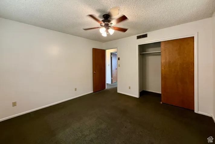 Unfurnished bedroom with dark carpet, a textured ceiling, a closet, and a ceiling fan