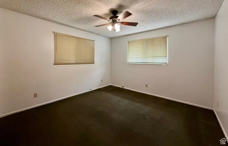 Spare room featuring dark carpet, a textured ceiling, and ceiling fan