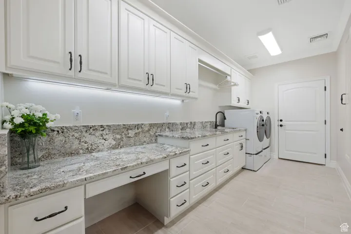Main Laundry room with granite countertops, soft-close cabinetry, cabinet space, and ornamental molding with built-in ironing board and entrance to garage.