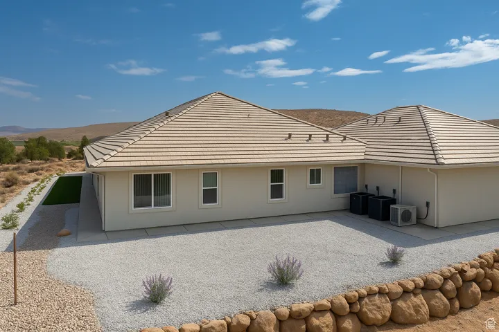 Rear view of house showing a tile roof and stucco siding with low maintenance landscaping.  Concrete sidewalks surround the home.
