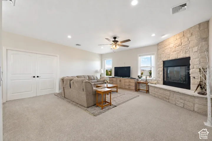 Living area featuring a floor-to-ceiling textured stone fireplace with a raised hearth, recessed lighting, double doors, and a ceiling fan