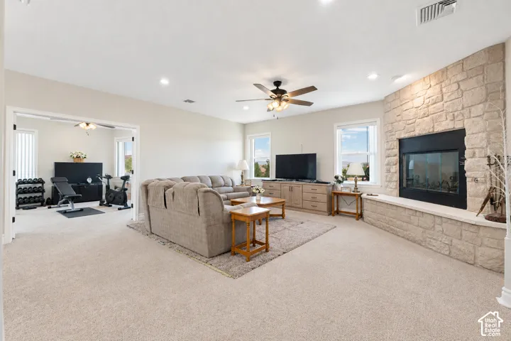 Spacious living area featuring neutral carpeting, a floor-to-ceiling stone fireplace, raised hearth, recessed lighting, and a ceiling fan