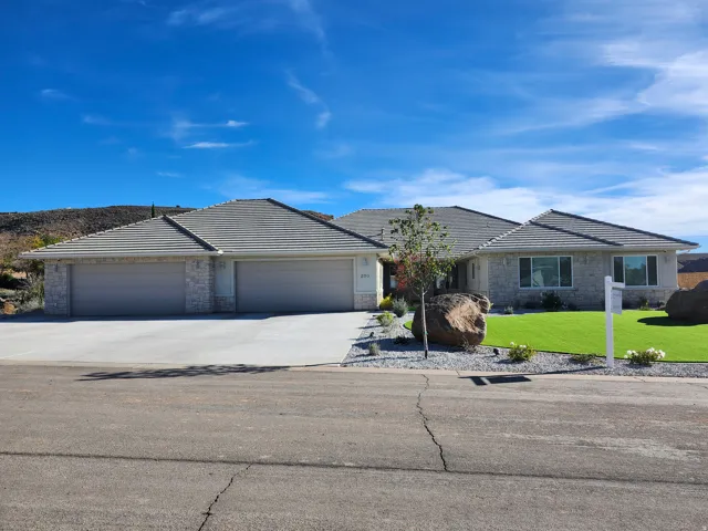 Single story home with driveway, a 5 car garage, a front lawn, and stone siding & night lighting.