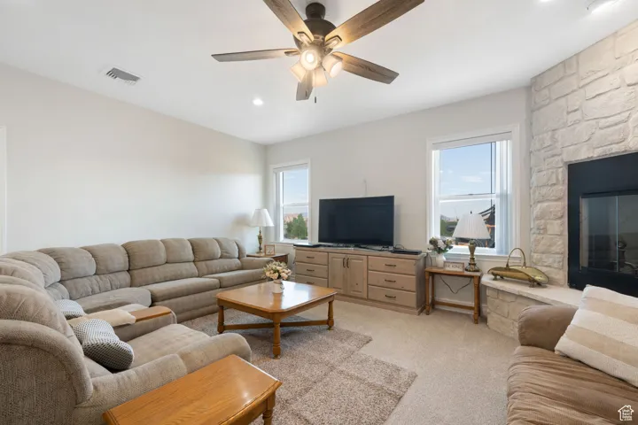 Main Family room with light colored carpet, healthy amount of natural light, a floor to ceiling stone fireplace, recessed lighting, ceiling fan and built in cabinet.