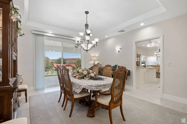 Main formal dining room featuring crown molding, a ceiling fan, sconces, recessed lighting, a tray ceiling, 3-tone paint and light colored carpet with sliding glass doors to the rear covered patio.