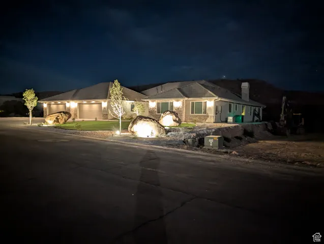 Ranch-style house with concrete driveway, a chimney, an attached 5+ car garage with two 18 ft doors, and stone siding plus exterior night lighting