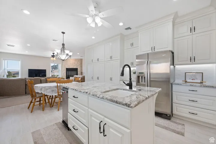 Main Gourmet Kitchen with a ceiling fan, stainless steel fridge, an island with sink, granite stone countertops, and recessed lighting plus nook with overhead fixture and family room with floor to ceiling stone fireplace with hearth.