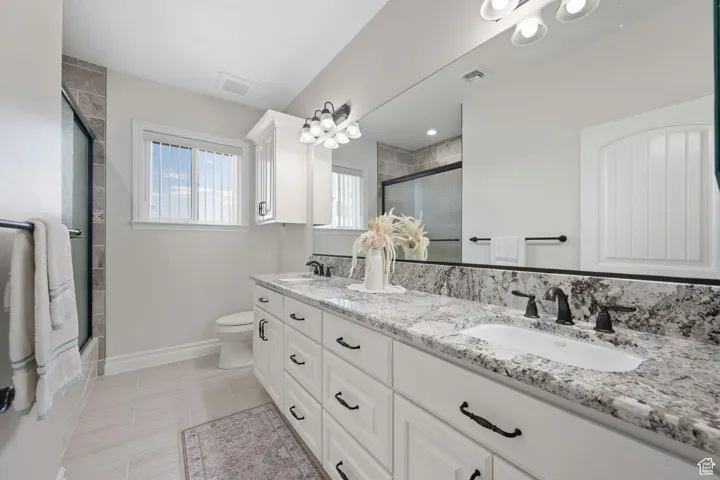 ADU Bathroom featuring double vanity and toilet, soft-close cabinetry, tile flooring, granite countertops, tile shower with sliding door.