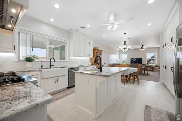 Main Gourmet Kitchen featuring extractor fan, decorative backsplash, a center island with sink & disposal, granite stone counters, recessed lighting & overhead fan.