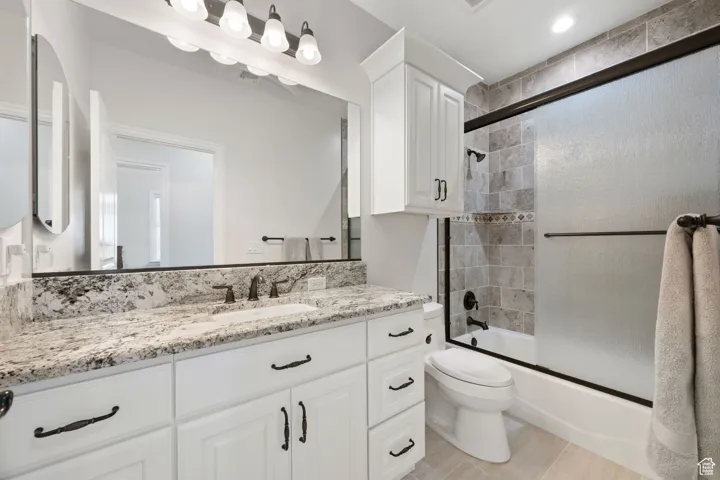 Full bath with vanity and shower / bath combination with sliding glass shower doors, granite countertops and soft-close cabinetry and tile flooring.