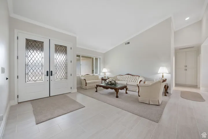 Main Entry / Living room featuring ornamental molding, french leaded-glass entry doors, high vaulted ceiling, and 3-tone paint, tile & carpet flooring