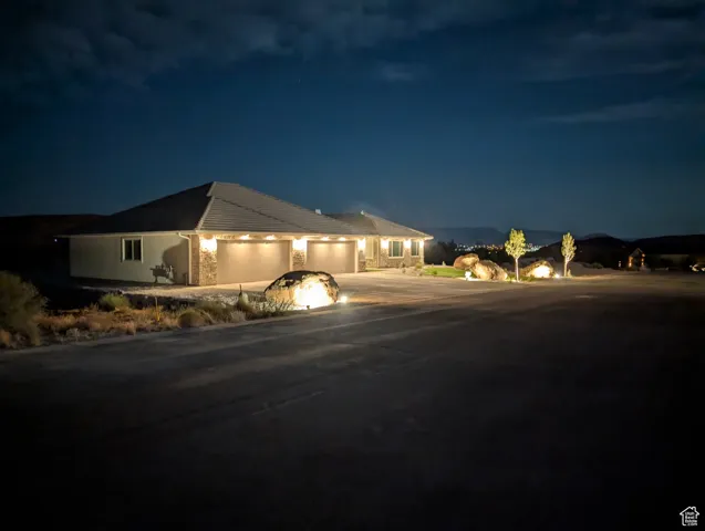 Single story home with a 5+ garage showing two 18' doors, concrete driveway and exterior night lighting