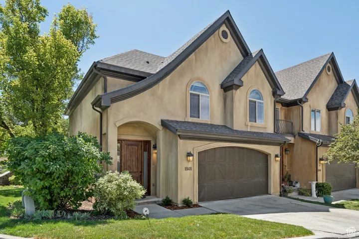 View of front facade featuring an attached garage, stucco siding, concrete driveway, and roof with shingles