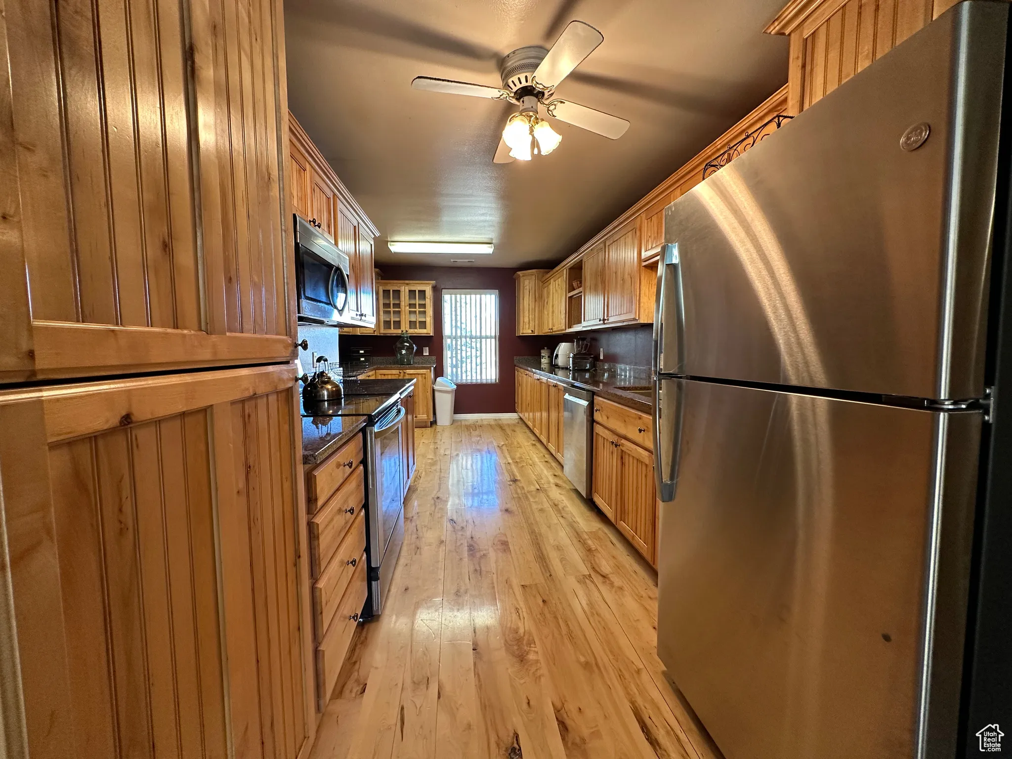 Kitchen with stainless steel appliances, light wood-style floors, brown cabinets, and glass insert cabinets