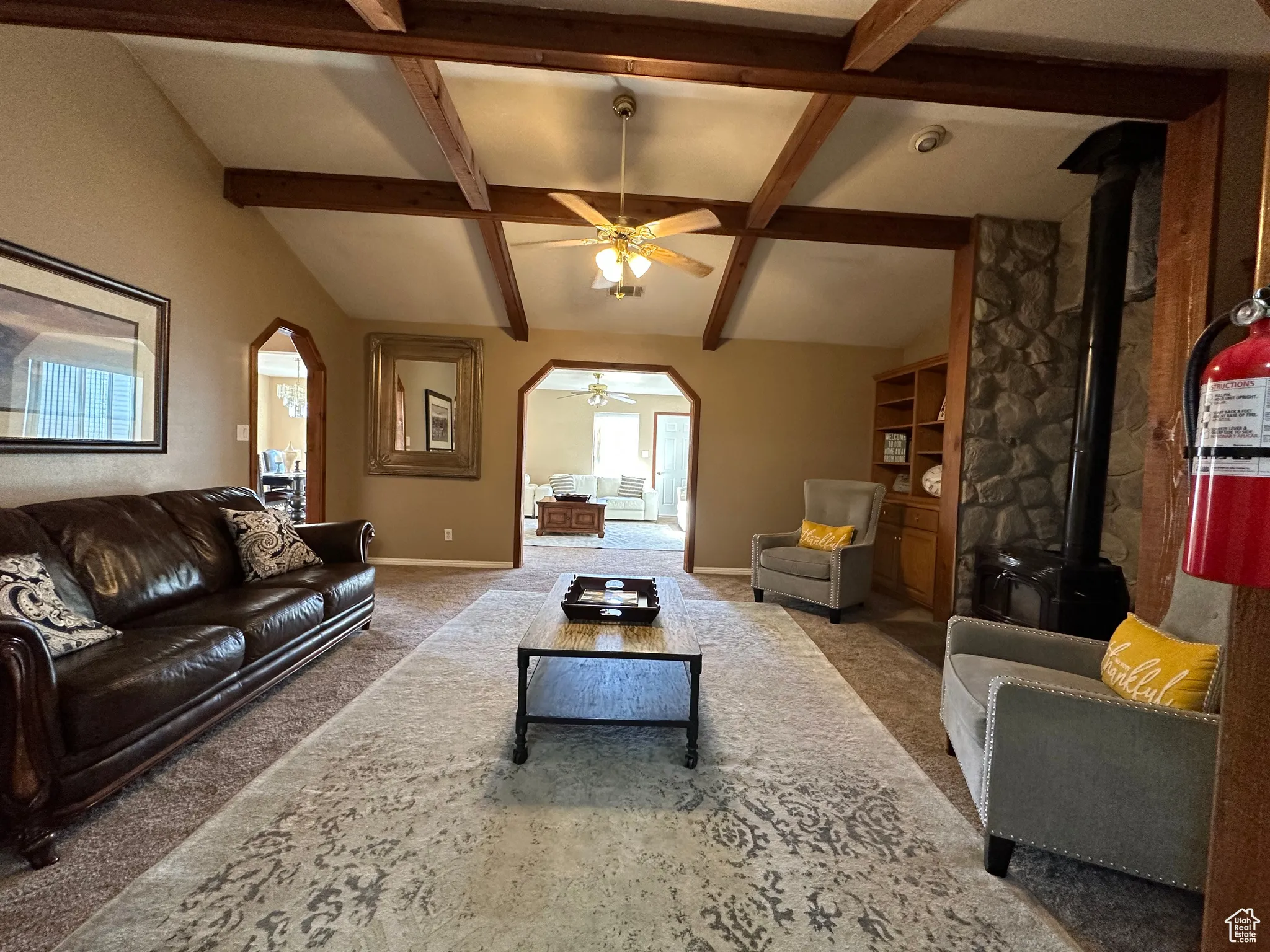 Living area with a wood stove, arched walkways, carpet, and ceiling fan
