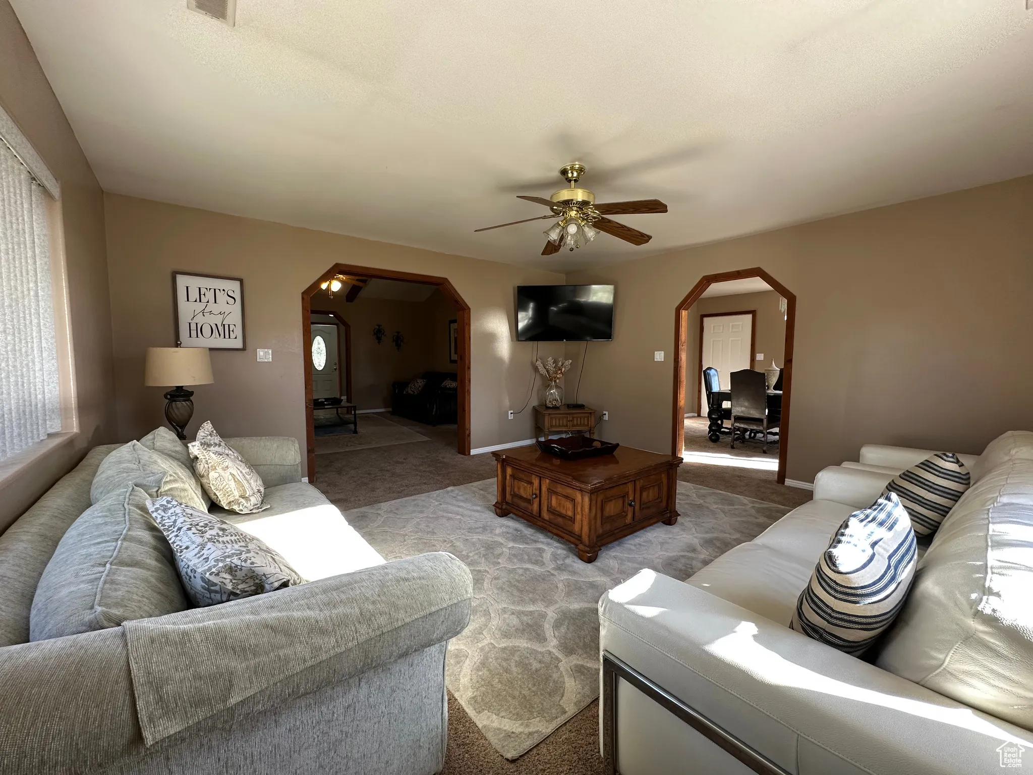 Living area with arched walkways, light colored carpet, a ceiling fan, and plenty of natural light