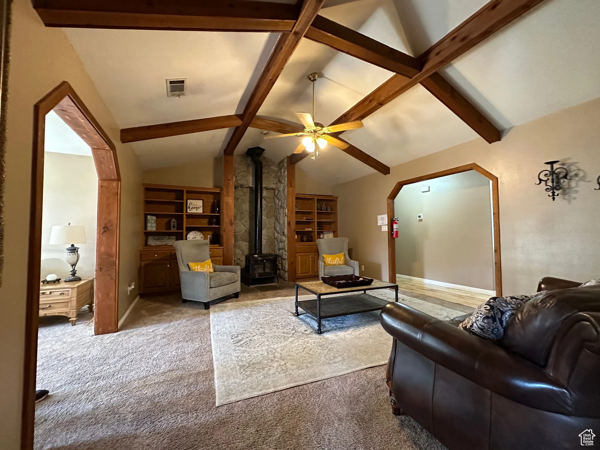 Living room with a wood stove, arched walkways, carpet floors, a ceiling fan, and built in features