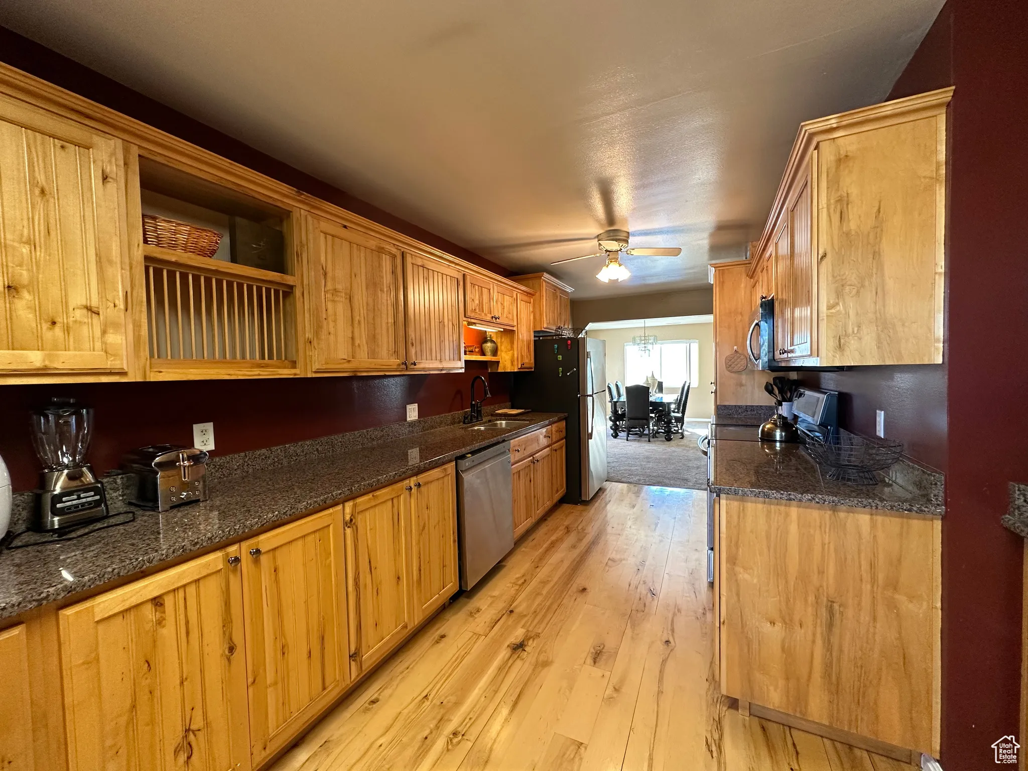 Kitchen featuring appliances with stainless steel finishes, light wood-style floors, dark stone countertops, a ceiling fan, and open shelves