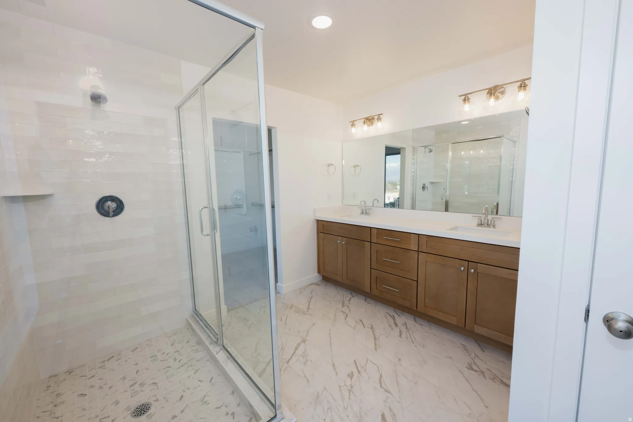 Full bathroom with a stall shower, double vanity, light marble finish floors, and recessed lighting
