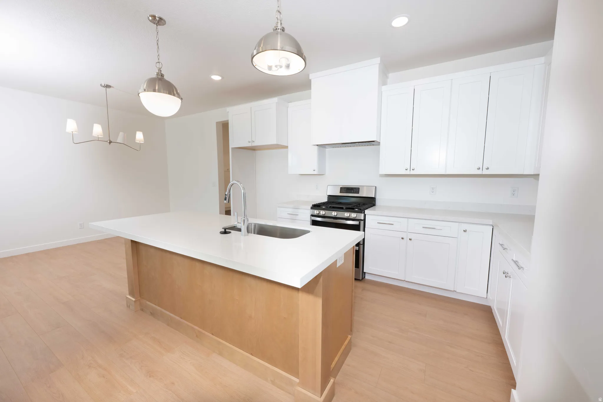 Kitchen with white cabinetry, stainless steel gas range, a kitchen island with sink, decorative light fixtures, and light wood finished floors