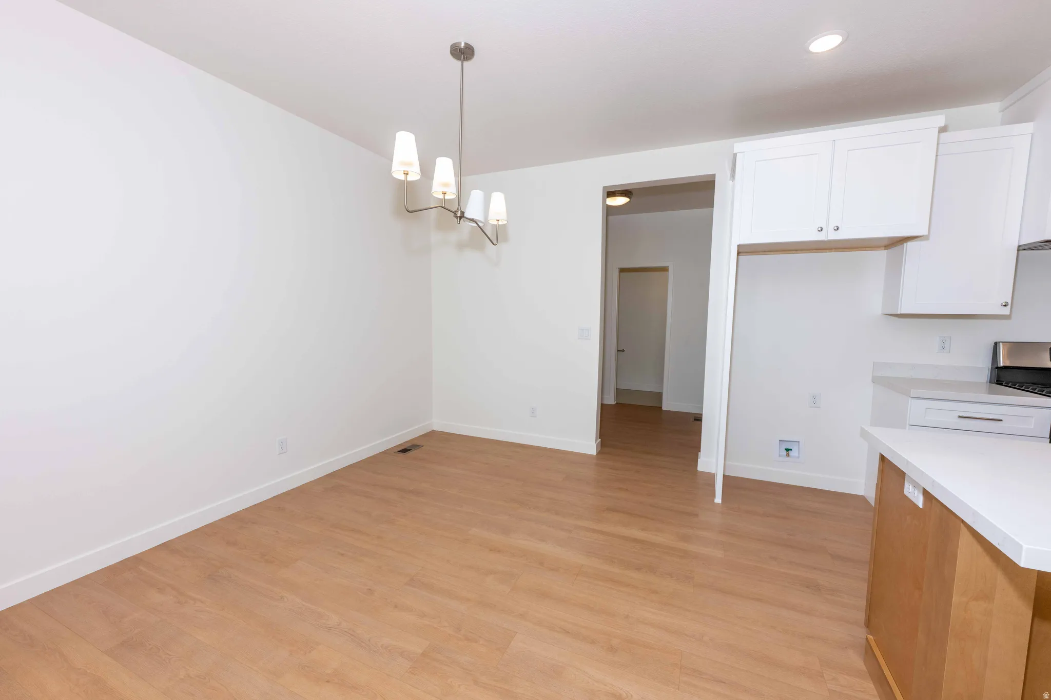 Kitchen featuring a chandelier, white cabinetry, light countertops, light wood finished floors, and hanging light fixtures