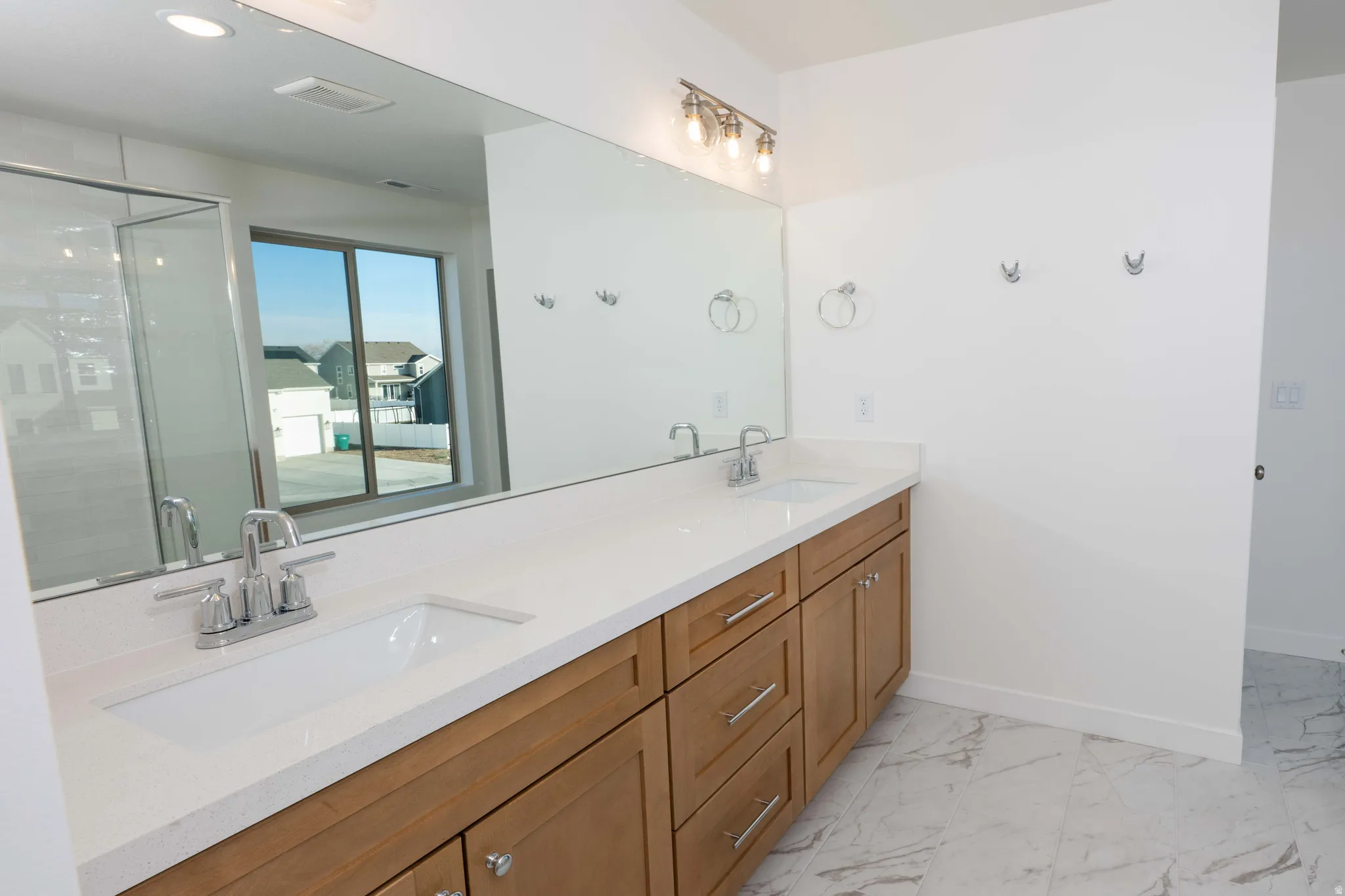 Full bath featuring double vanity, a shower stall, and light marble finish floors