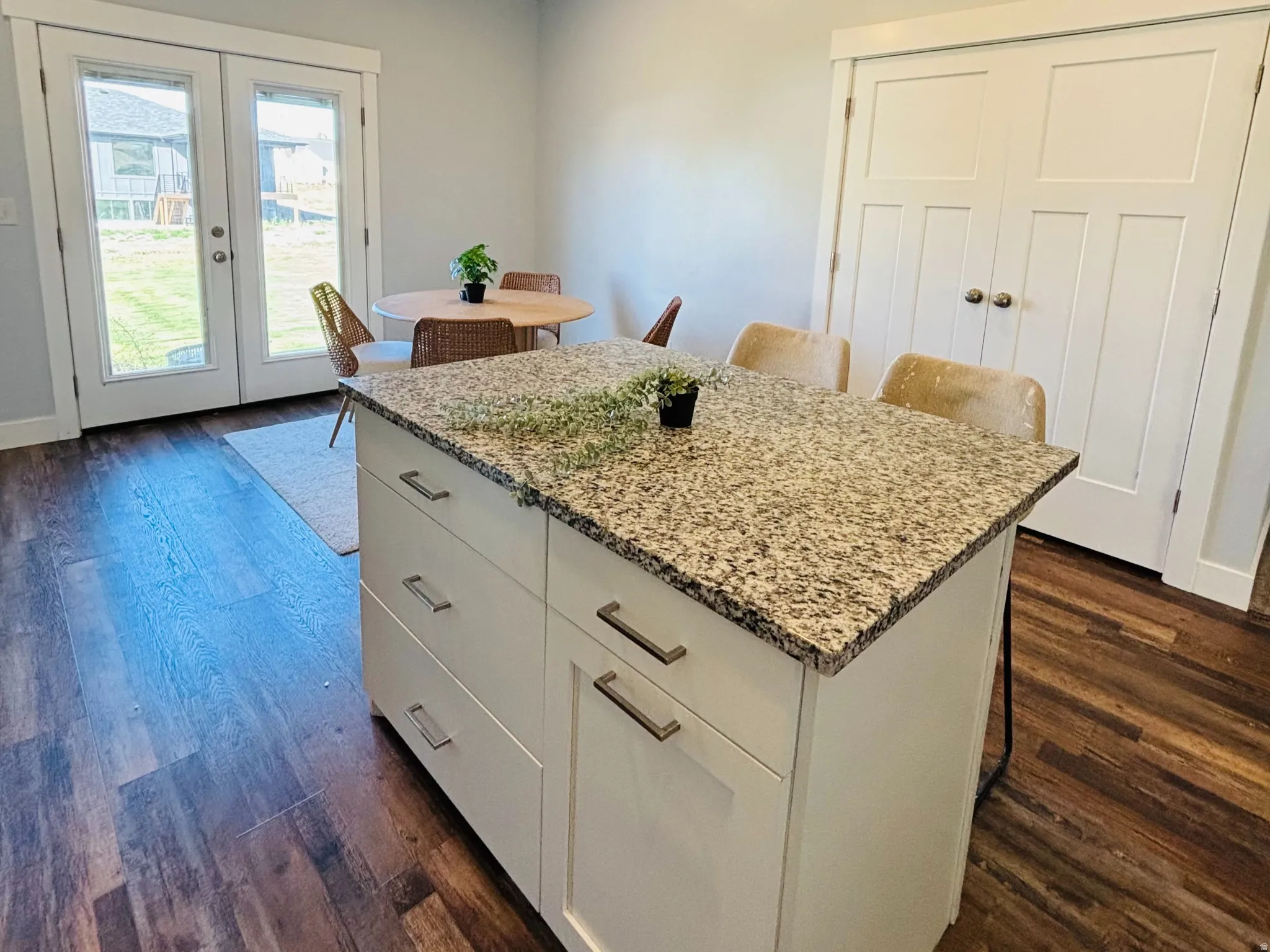Kitchen with a kitchen bar, white cabinetry, light stone counters, dark wood finished floors, and french doors