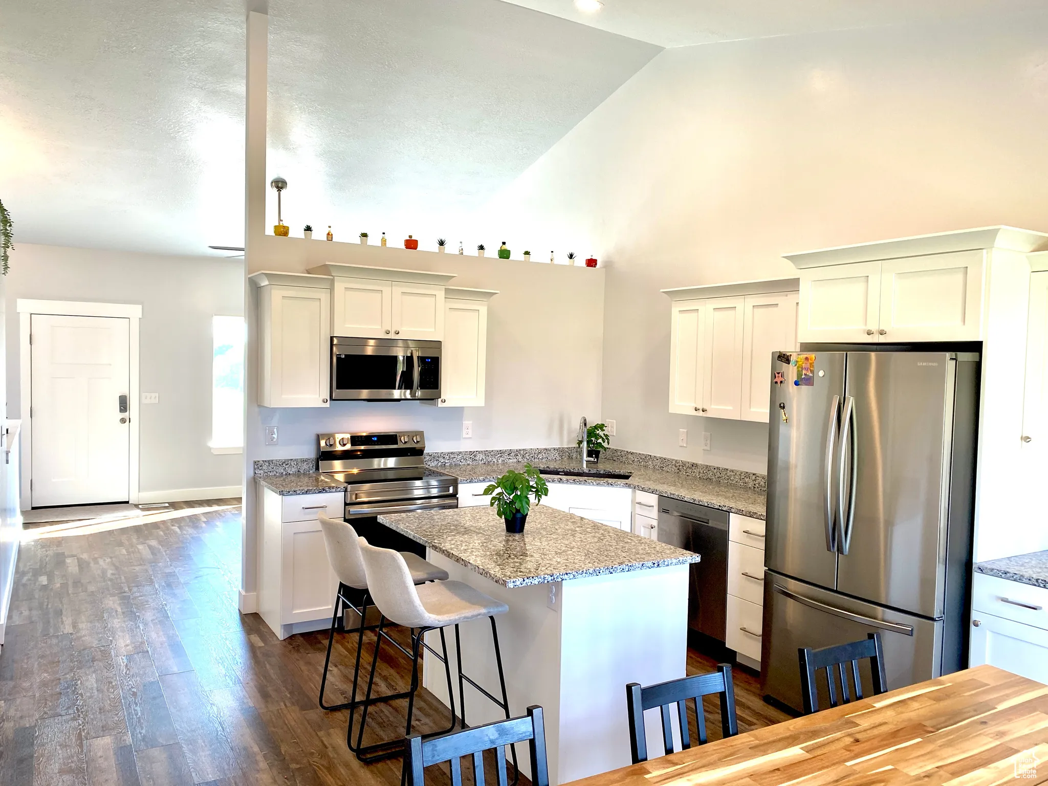 Kitchen featuring appliances with stainless steel finishes, dark wood-style floors, a bar / island center  and granite stone counters