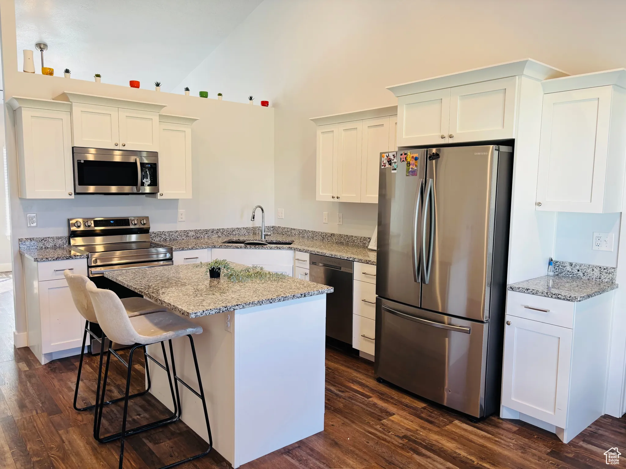 Kitchen featuring appliances with stainless steel finishes, light stone counters, white cabinetry, dark wood-type flooring, and a kitchen bar