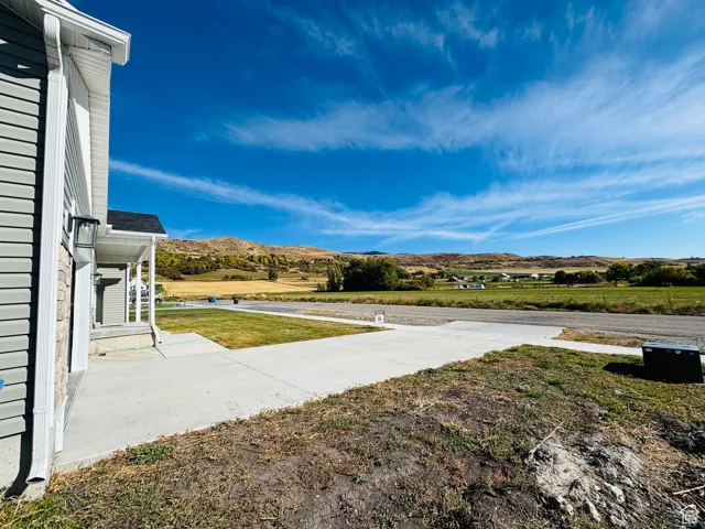 West side of house, driveway and porch, looking west across an open field, to the east,