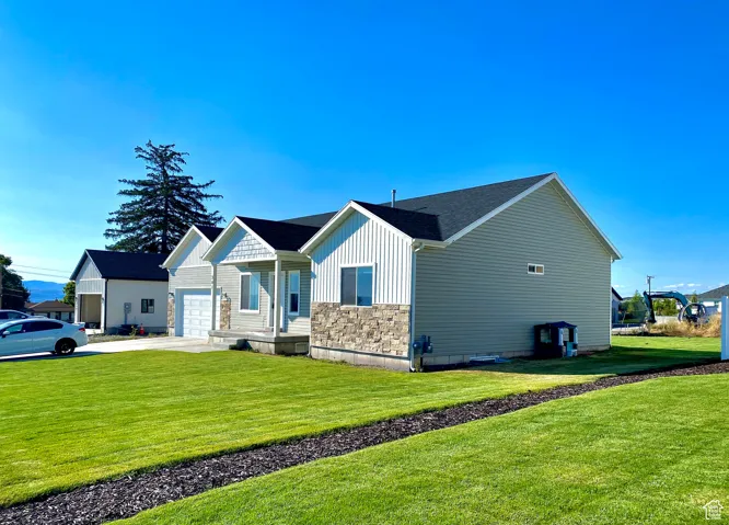 View of home's exterior featuring board and batten siding, stone siding, a lawn, driveway, and a garage. Faces South.