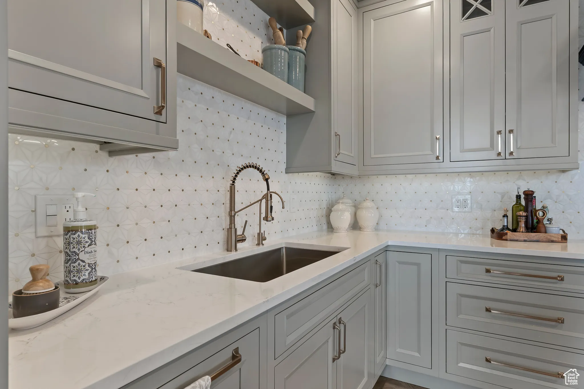 Kitchen featuring tasteful backsplash, gray cabinets, light stone countertops, and open shelves