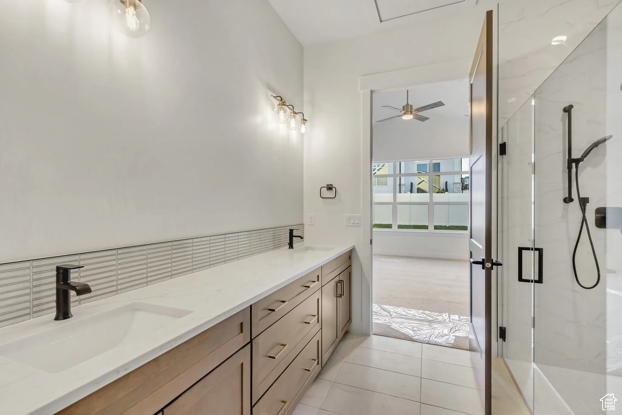 Full bath with a marble finish shower, double vanity, light tile patterned floors, and a ceiling fan