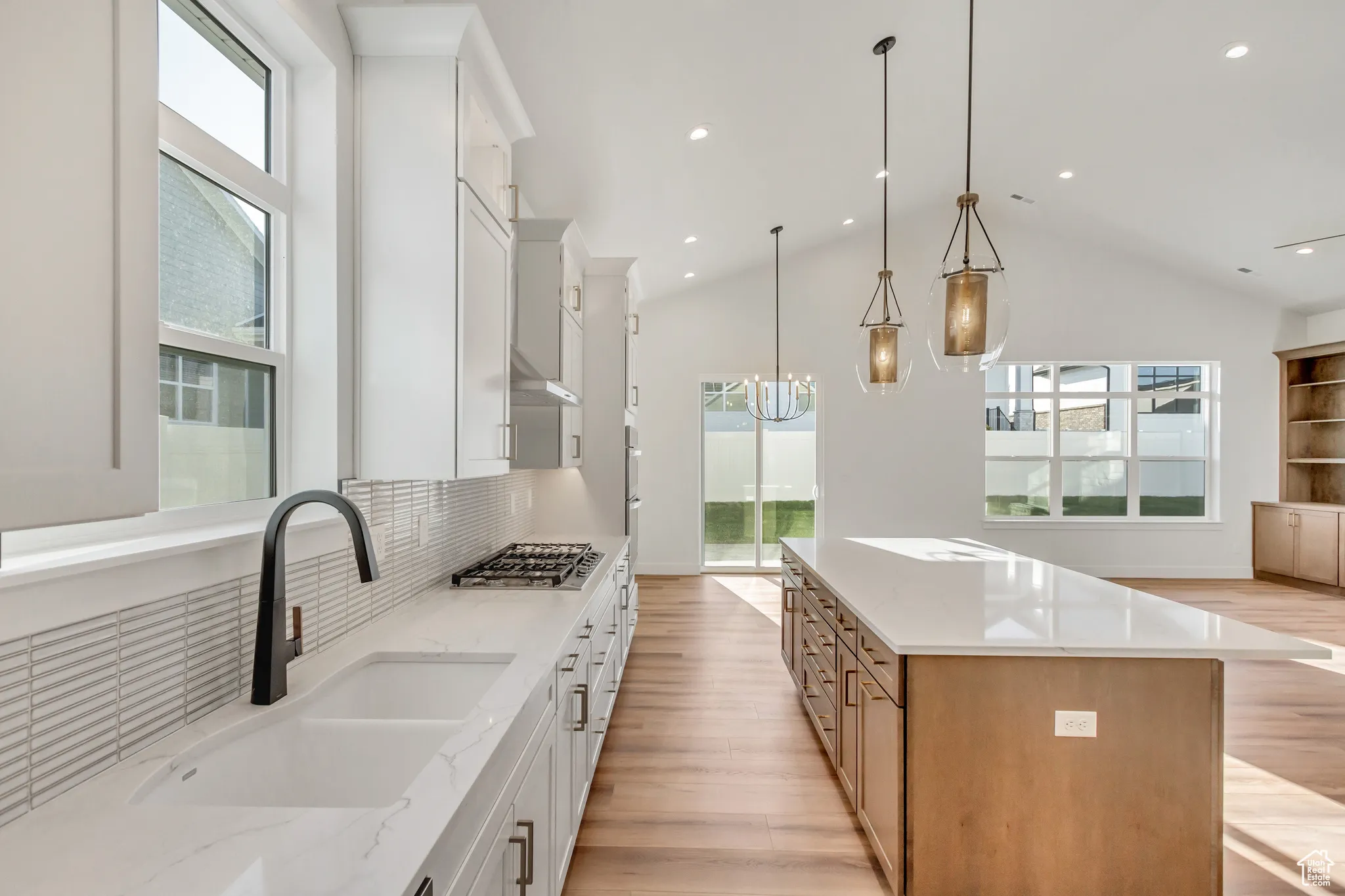 Kitchen with a large island, light stone counters, white cabinets, decorative light fixtures, and light wood-style floors