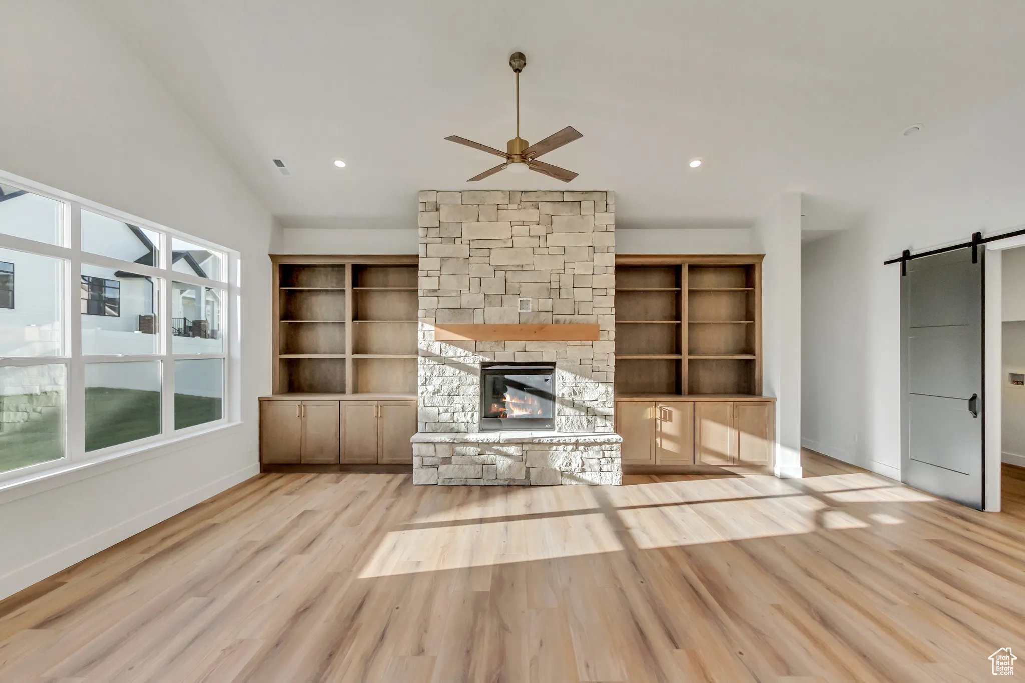 Unfurnished living room featuring a barn door, ceiling fan, light wood-style flooring, a fireplace, and recessed lighting