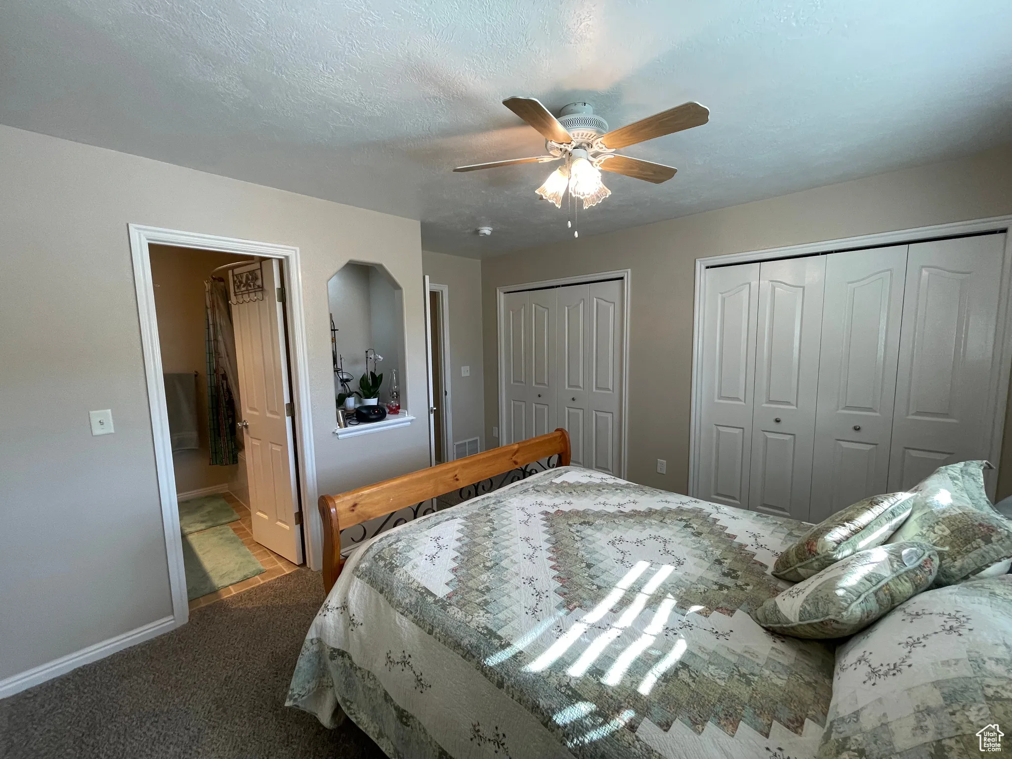 Bedroom featuring two closets, carpet, a textured ceiling, a ceiling fan, and ensuite bathroom