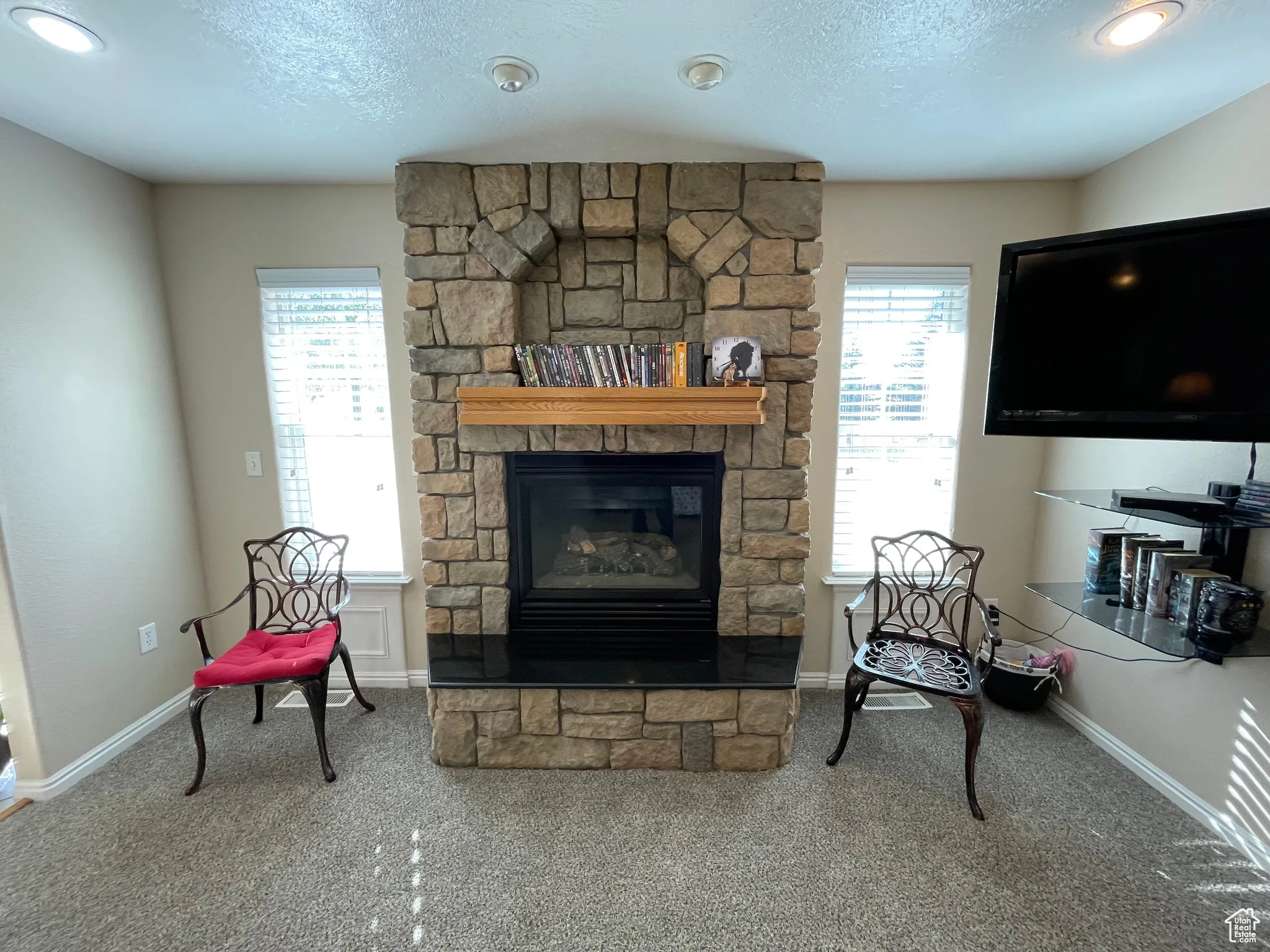 Living area featuring carpet floors, a stone fireplace, a textured ceiling, and recessed lighting