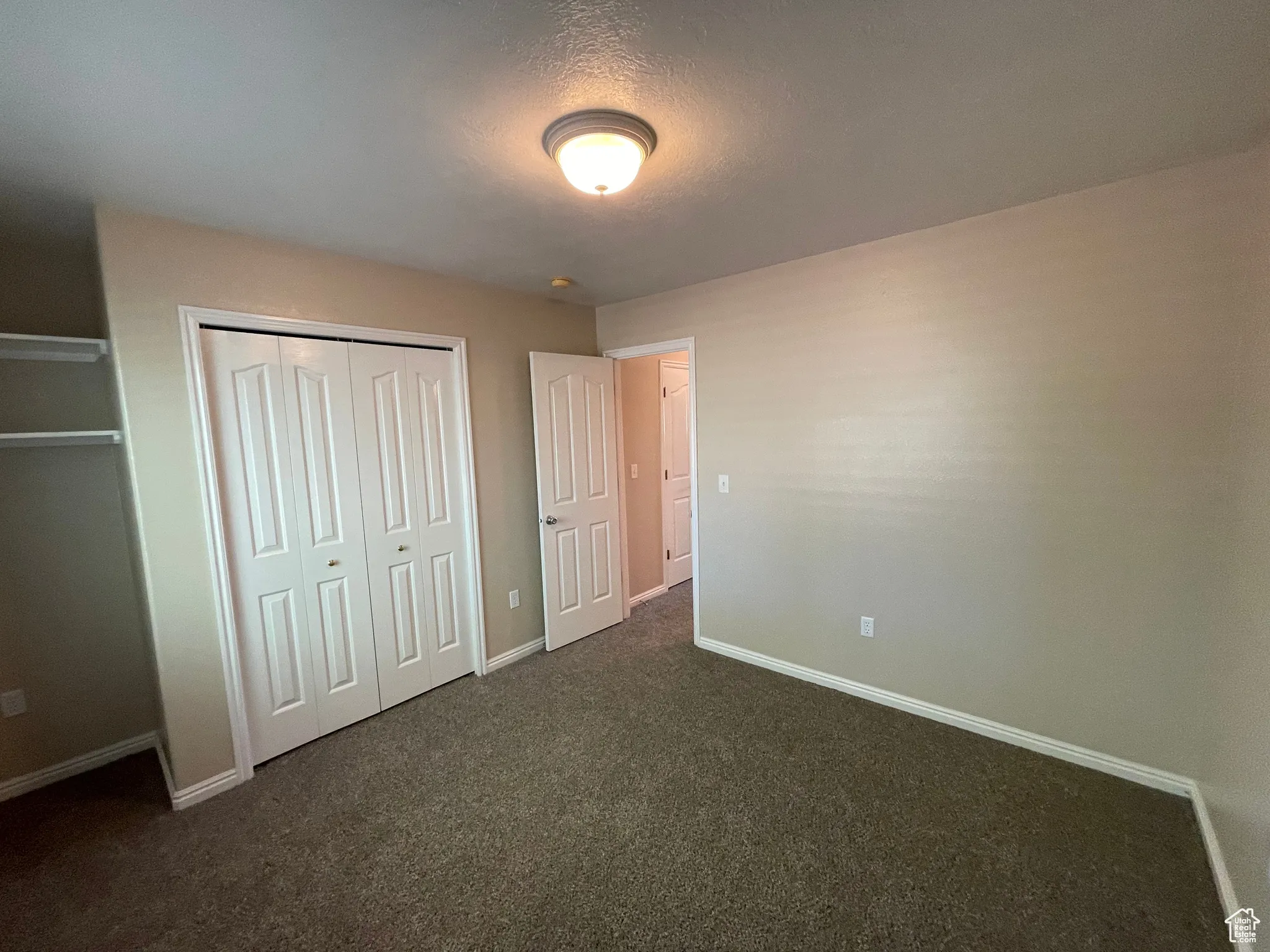 Unfurnished bedroom featuring dark colored carpet, a textured ceiling, and a closet