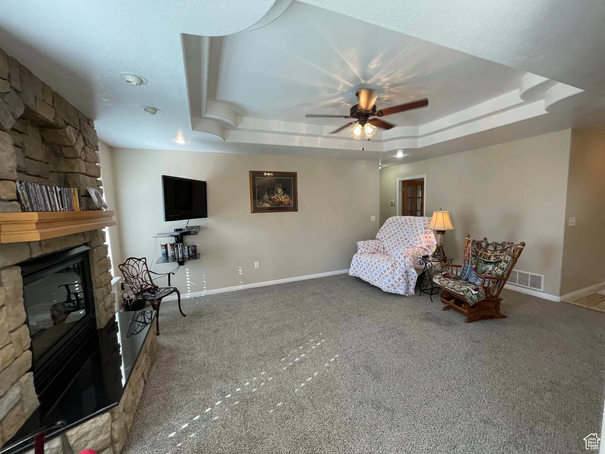 Sitting room with a stone fireplace, carpet, and a raised ceiling