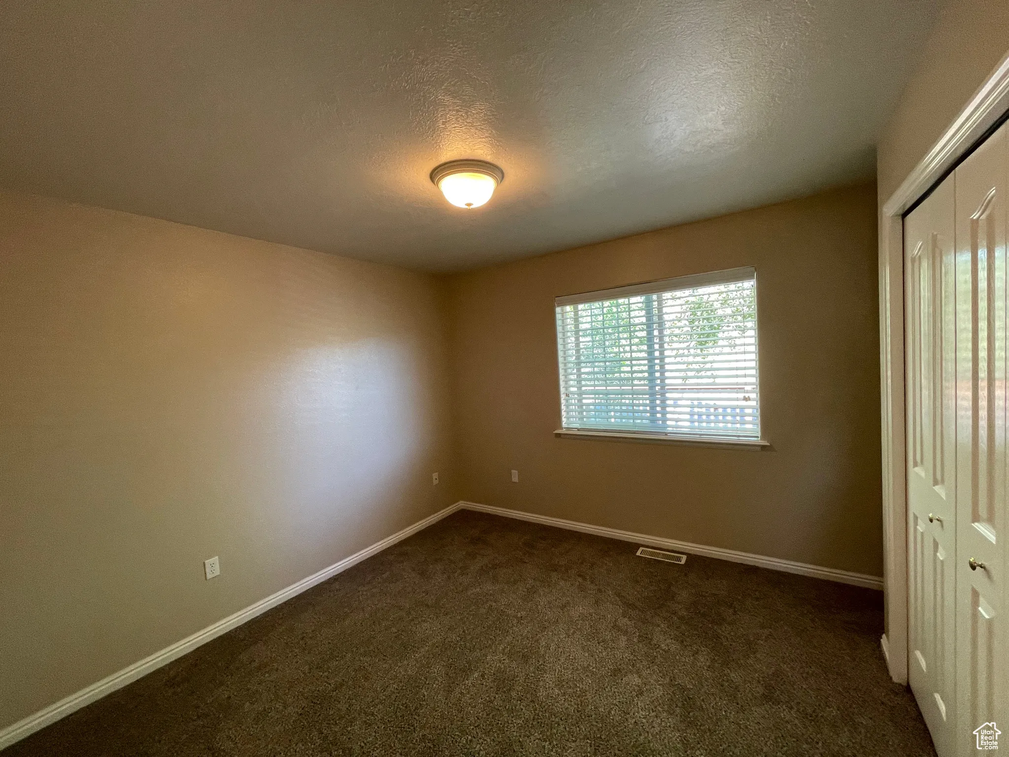 Unfurnished bedroom featuring a closet, dark carpet, and a textured ceiling