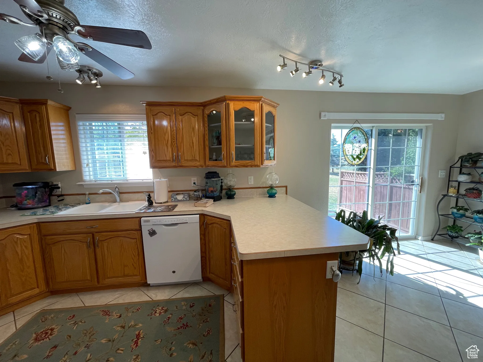 Kitchen featuring a peninsula, light tile patterned flooring, dishwasher, a textured ceiling, and brown cabinets