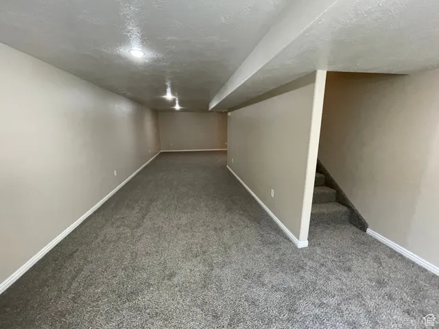 Finished below grade area featuring a textured ceiling, carpet floors, and stairs